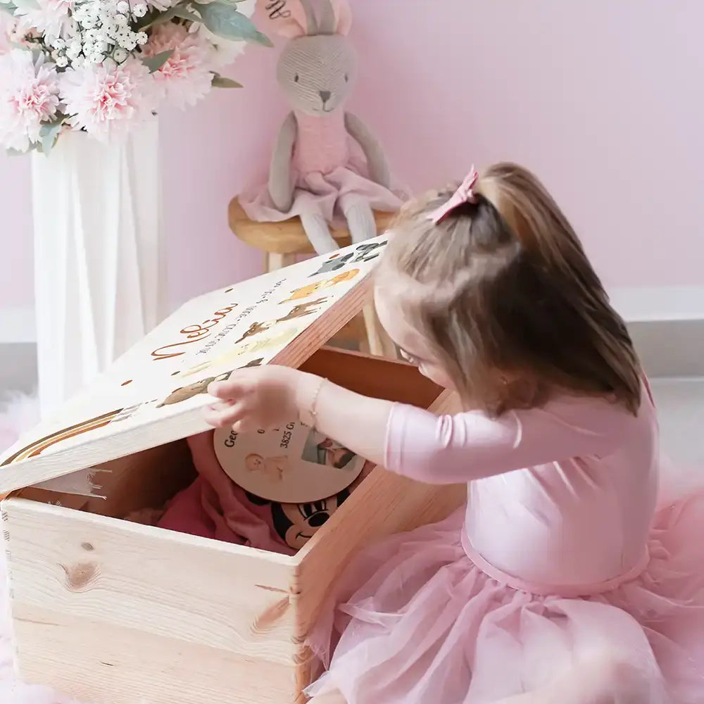 Mädchen betrachtet liebevoll personalisierte Erinnerungsbox zur Geburt mit Waldtieren - einzigartiges Babygeschenk in Rosa