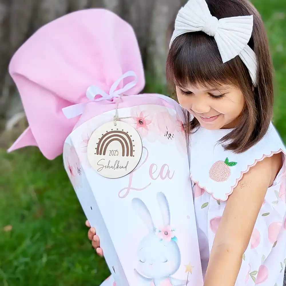 Personalisierte Schultüte für Mädchen mit Hasen-Motiv und Namen 'Lea'. Lächelndes Schulkind 2025 mit rosa Zuckertüte zur Einschulung. Perfektes Geschenk zum Schulanfang mit individuellem Holzanhänger.